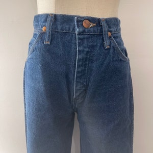 Pu&ograve; includere: Un paio di jeans blu denim con un bottone e rivetti in rame. I jeans hanno vita alta e gamba dritta.