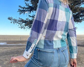 Puede incluir: Una camisa de manga larga con estampado de cuadros azules, verdes y blancos con un corte corto.