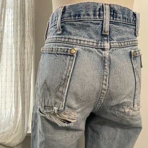 May include: Light blue denim jeans with a distressed look. The jeans have a ripped hole on the left back pocket and a small rip on the right back pocket.