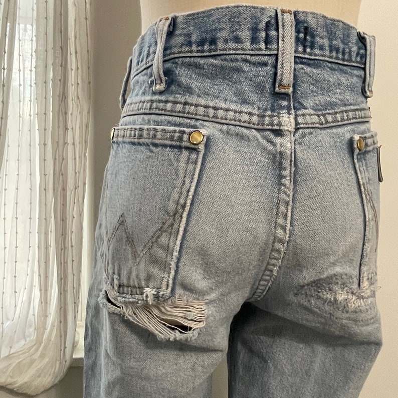 May include: Light blue denim jeans with a distressed look. The jeans have a ripped hole on the left back pocket and a small rip on the right back pocket.