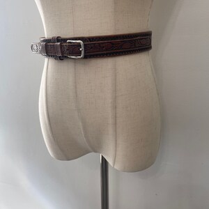 May include: A brown leather belt with an intricate floral design and a silver buckle.