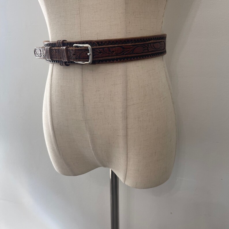 May include: A brown leather belt with an intricate floral design and a silver buckle.