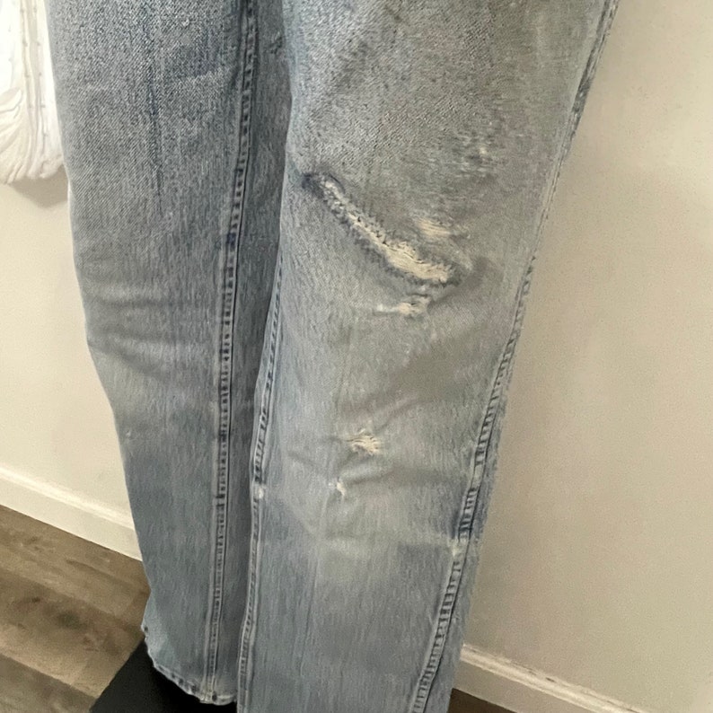 May include: Light blue denim jeans with distressed details and fading. The jeans have several small holes and tears on the front of the right leg.