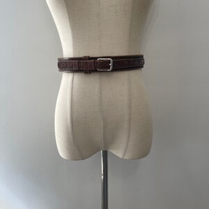 May include: A brown leather belt with an intricate floral design and a silver buckle.