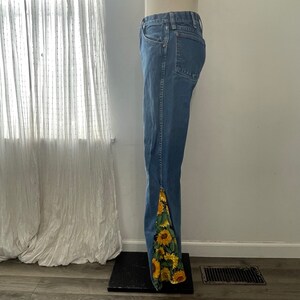 以下が含まれることがあります： 裾にひまわり柄の青いデニムジーンズです。
