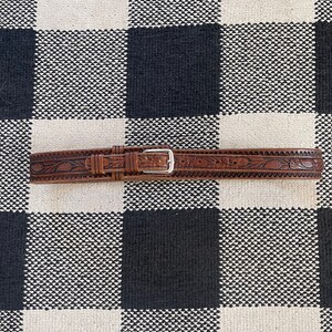 May include: A brown leather belt with an intricate floral design and a silver buckle.