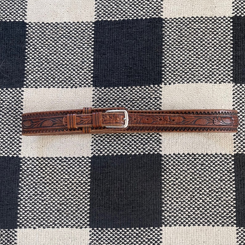May include: A brown leather belt with an intricate floral design and a silver buckle.