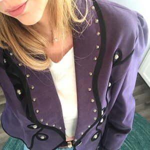 May include: A purple blazer with black trim and silver accents. The blazer has a pointed collar and a single button closure.