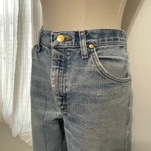 May include: Light blue denim jeans with a faded look and gold button accents.