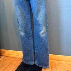 May include: Faded blue denim jeans with light distressing on the knees. The jeans have a classic five-pocket design and a straight leg cut. The denim has a worn appearance.