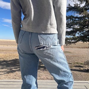 May include: Light blue denim jeans with a distressed tear on the back pocket. The jeans have a classic five-pocket design and a straight leg fit. The person is wearing a gray sweatshirt.