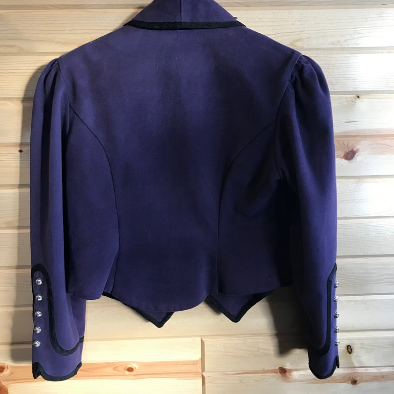 May include: A purple cropped jacket with black trim and silver buttons on the cuffs. The jacket has a scalloped hem.