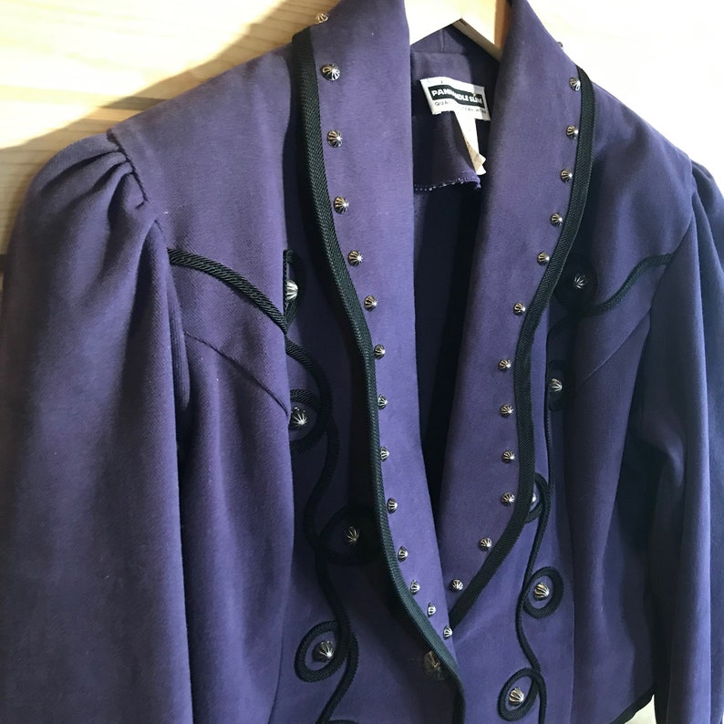 May include: A purple jacket with black trim and silver studs. The jacket has a western-style design with embroidered details.