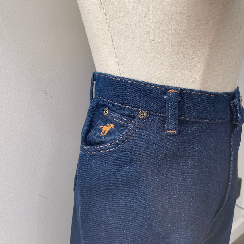 May include: Dark blue denim skirt with a small horse logo embroidered on the front pocket.