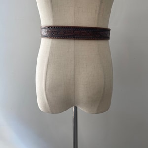 May include: A brown leather belt with an intricate floral design. The belt is on a white mannequin.