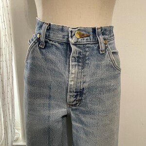May include: Light blue denim jeans with a high waist and a button fly. The jeans have a faded look and are made of a soft, comfortable material.