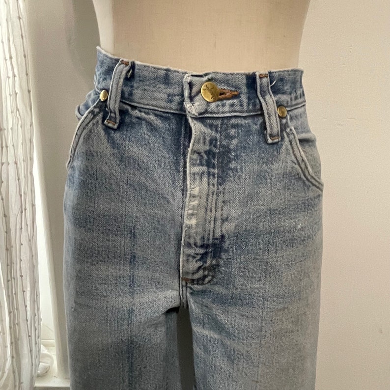 May include: Light blue denim jeans with a high waist and a button fly. The jeans have a faded look and are made of a soft, comfortable material.