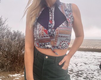 May include: A sleeveless crop top with a geometric pattern in shades of red, blue, white, and black. The top has a tie at the front and a collar.