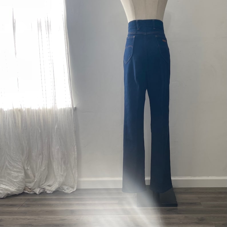 May include: A pair of dark blue denim jeans with a high waist and a straight leg fit. The jeans have a classic five-pocket design and a button fly.