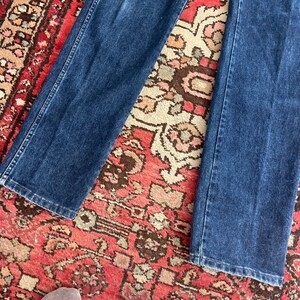 May include: Dark blue denim jeans. The jeans have a classic five-pocket design, with a straight leg cut. The denim is a medium weight, and the jeans appear to be well-worn.