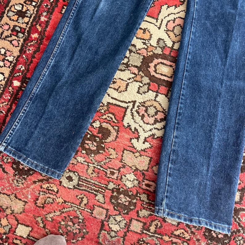 May include: Dark blue denim jeans. The jeans have a classic five-pocket design, with a straight leg cut. The denim is a medium weight, and the jeans appear to be well-worn.