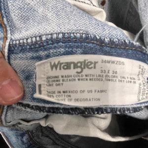 May include: A white Wrangler jeans care label with the text "36MWZDS", "33 x 36", "Machine wash cold with like colors, only non-chlorine bleach when needed, tumble dry low or line dry", "Made in Mexico of US fabric", "100% cotton", and "Exclusive of decoration".