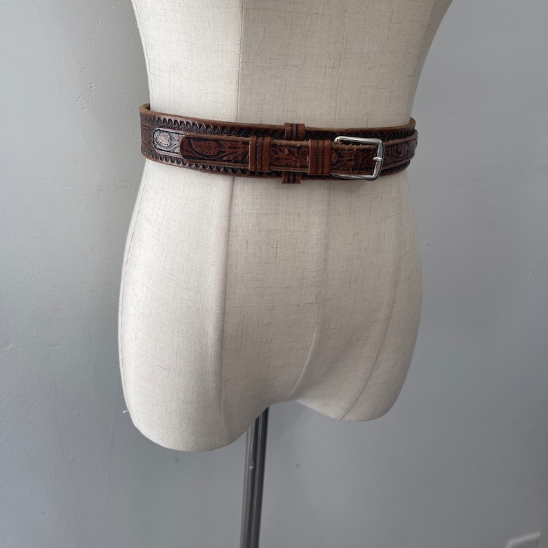 May include: A brown leather belt with an intricate floral design and a silver buckle.