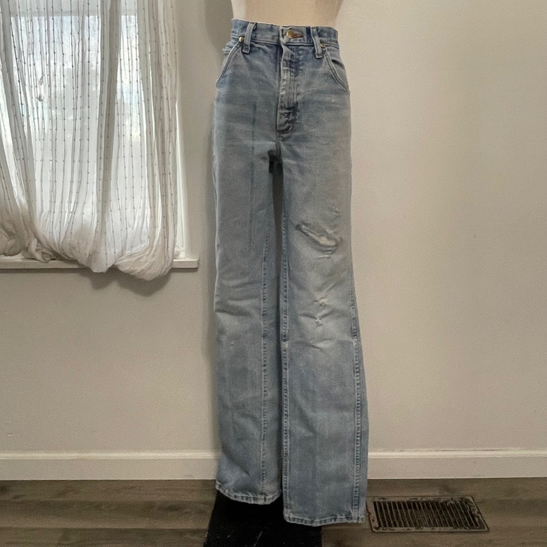 May include: Light blue denim jeans with a wide leg and a high waist. The jeans have a faded look and some distressing.