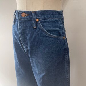 Pu&ograve; includere: Un paio di jeans in denim blu scuro con un bottone e rivetti in rame. I jeans hanno uno stile classico a cinque tasche.