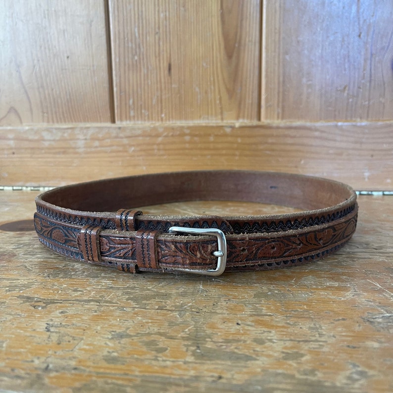 May include: A brown leather belt with an intricate floral design and a silver buckle.