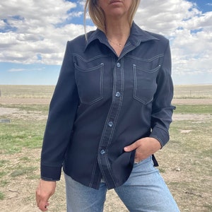 May include: A navy blue long-sleeved shirt with white stitching detail. The shirt has a collared neckline, button closure, and two chest pockets.