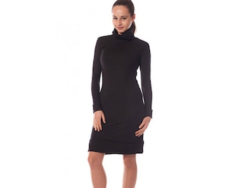 May include: A black long-sleeve dress with a turtleneck collar. The dress has a fitted silhouette and falls to the mid-thigh. The model is wearing black high-heeled shoes.