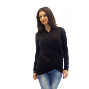 May include: A woman wearing a black long-sleeved wrap top with a button detail and blue jeans.