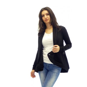 May include: A black cardigan with a long, flowing design and a single button closure. The cardigan is worn over a white t-shirt and blue jeans.