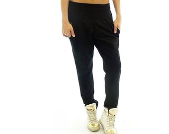 May include: Black pants with a low rise and a relaxed fit. The pants have a gold zipper detail on the front. The model is wearing white high-top sneakers.