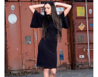 May include: A black turtleneck dress with long sleeves and a flared hem. The dress is knee-length and has a fitted silhouette. The model is wearing the dress with black heels.
