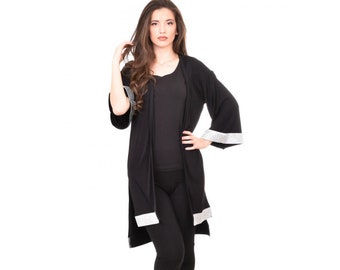 May include: A black long-sleeved cardigan with a white trim around the edges. The cardigan is worn over a black tank top and black pants.