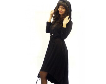 May include: A black hooded dress with a long, flowing skirt and a high neckline. The dress has a cinched waist and a tie at the front. The model is wearing black boots.