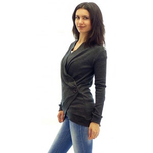 May include: A dark gray wrap cardigan with a single button closure. The cardigan is made of a soft, knitted fabric and has a relaxed fit.