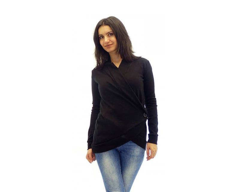 May include: A woman wearing a black long-sleeved wrap top with a button detail and blue jeans.