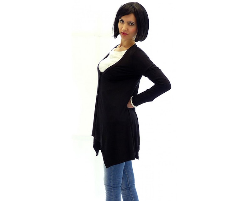 Peut inclure: Un cardigan noir &agrave; manches longues avec un col en V et une ourlet l&eacute;g&egrave;rement asym&eacute;trique. Le cardigan est port&eacute; sur un t-shirt blanc et un jean bleu.
