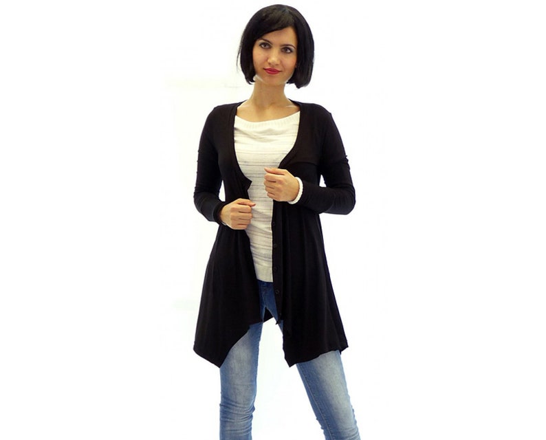 Peut inclure: Un cardigan noir &agrave; manches longues avec un devant drap&eacute; et une fermeture boutonn&eacute;e. Le cardigan est port&eacute; sur une chemise blanche &agrave; rayures et un jean bleu.
