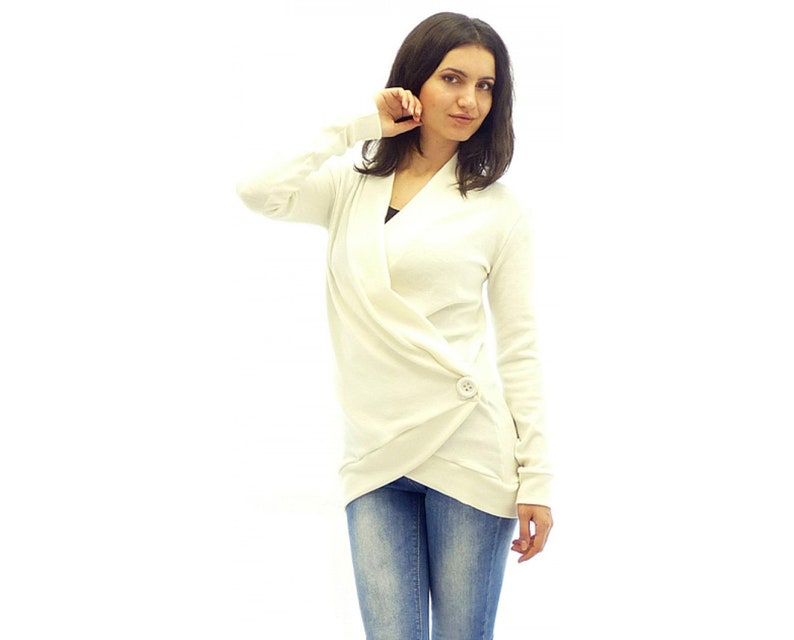 May include: A white wrap cardigan with a single button closure. The cardigan is made of a soft, knit fabric and has a relaxed fit.