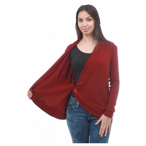 May include: A burgundy cardigan with a single button closure. The cardigan is open in the front, revealing a black undershirt. The model is wearing blue jeans.