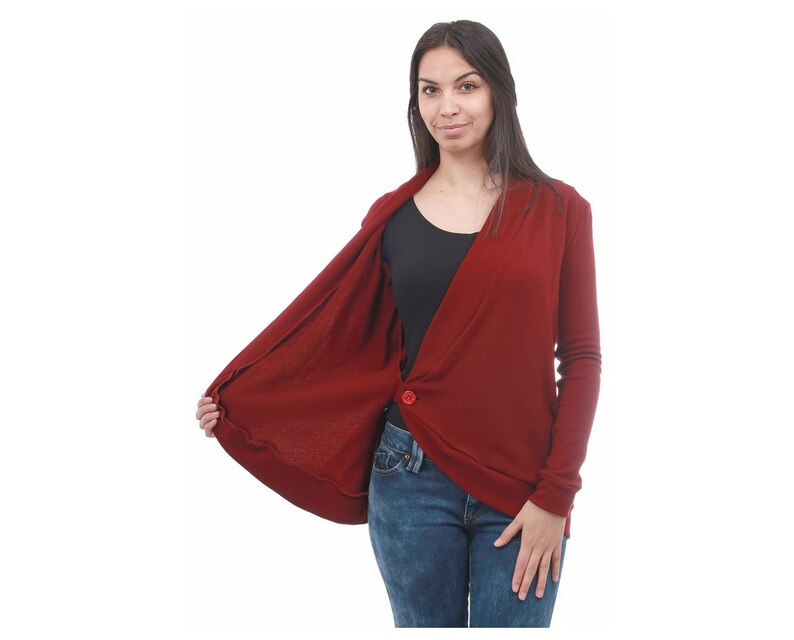 May include: A burgundy cardigan with a single button closure. The cardigan is open in the front, revealing a black undershirt. The model is wearing blue jeans.