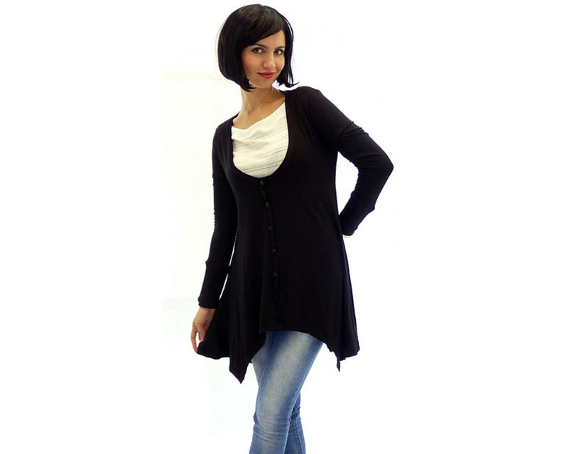 Peut inclure: Un cardigan noir &agrave; manches longues avec un devant boutonn&eacute; et une ourlet l&eacute;g&egrave;rement asym&eacute;trique. Le cardigan est port&eacute; sur une chemise blanche et un jean bleu.