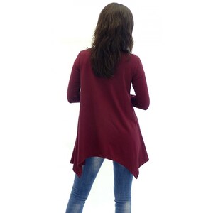 Peut inclure: Un chemisier &agrave; manches longues de couleur bordeaux avec une coupe asym&eacute;trique. Le chemisier est fait d'un tissu doux et extensible et a une coupe d&eacute;contract&eacute;e.