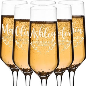 Puede incluir: Seis copas de champ&aacute;n llenas de un l&iacute;quido dorado brillante. Cada copa est&aacute; personalizada con un nombre, un rol y una fecha en una fuente blanca, con detalles florales. Las copas son para una boda.