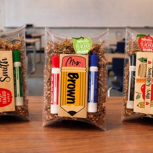 May include: Three clear cellophane bags filled with shredded paper, each containing a wooden teacher gift. Each gift includes dry-erase markers and a personalized wooden sign. The signs read "Mrs. Smith", "Brown", and "Mrs. Williams".