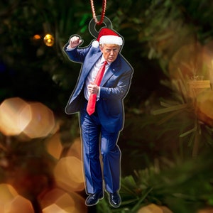 May include: A Christmas ornament featuring a person wearing a blue suit, red tie, and a Santa hat. The ornament is hanging from a Christmas tree.